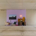 Zu sehen ist der Rohbau eines Bürokomplexes von SIGNA in Berlin, in dem Parasite Real Estate eine Intervention gestartet hat. Es wurde ein Teil der Wand und Boden in einem hellviolet gestrichen und Möbel a la einer Ein-Zimmer Wohnung auf die Fläche gestellt.